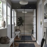 Modern entryway with glass-walled closet, featuring sliding doors, white decor, and potted plant.