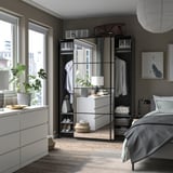 Modern bedroom with PAX wardrobe, mirrored sliding doors, white drawers, bed with grey linens, plants, and city view.