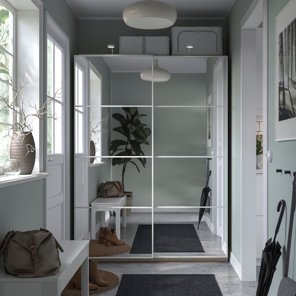 Modern entryway with gray PAX closet, glass doors, white pendant lights, potted plant, beige purse, black umbrellas, gray rugs, and stylish decor.