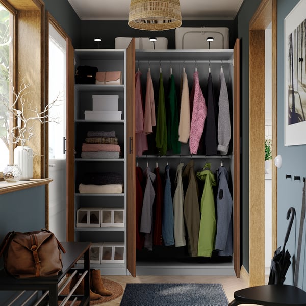 Open wardrobe displaying clothes on hangers, folded sweaters, and storage boxes. A handbag and umbrella stand are nearby.