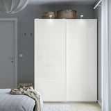 Minimalist bedroom with large white PAX wardrobe, sliding doors, grey walls, and bed with beige blanket.