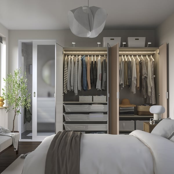 Modern bedroom with open wardrobe showing clothes, shelves, and drawers. Integrated lighting highlights stored items.