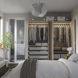Modern bedroom with open wardrobe showing clothes, shelves, and drawers. Integrated lighting highlights stored items.