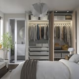 Modern bedroom with open wardrobe showcasing clothes, shelves, and organizers. Soft lighting and mirror doors enhance space.