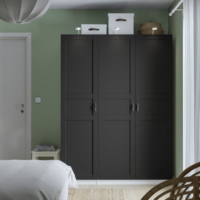 Modern bedroom with large black PAX wardrobe, white bed, green walls, and hanging wicker basket.
