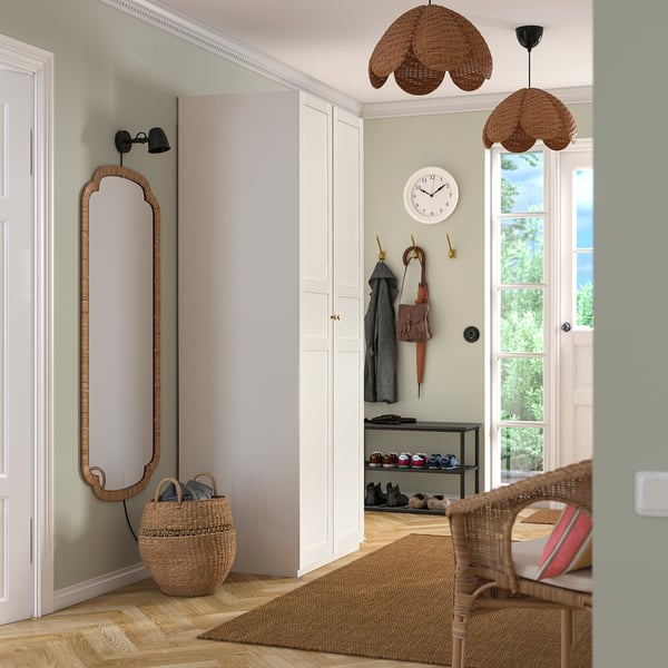 Light-filled entryway with mirror, hooks, baskets, and shoe shelf. Full-length mirror beside closet, clock above hooks. Natural, rustic design.