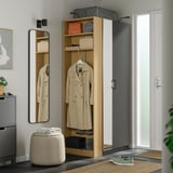 A PAX wardrobe with hanging coat, shelves, and mirror. The wardrobe is tall, grey, and sleek, fitting neatly in a corner next to a white door.
