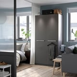 Modern apartment bedroom with dark gray PAX wardrobe, white bed, large windows, and wooden floor.