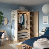 Cozy bedroom with blue walls, a modern PAX wardrobe with clothes, and a bed with toys and a plant.