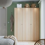 Large wooden closet with mirror doors stands tall against green wall, nearly touching the ceiling, beside narrow door and bed.