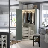 An open wardrobe with clothes hangers, drawers, and baskets inside. The closed green door hides storage when closed.