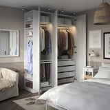 Bedroom with open wardrobe showing hanging clothes, shelves, and drawers. Soft lighting illuminates the organized space.