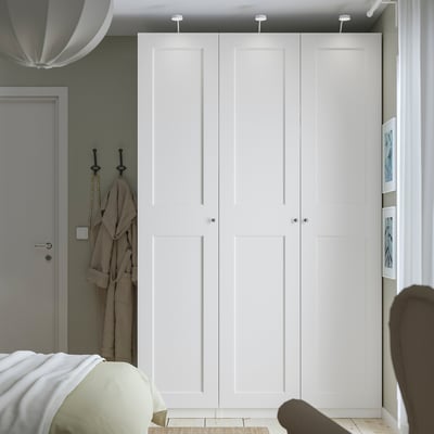 Minimalist bedroom with large white PAX wardrobe, silver knobs, grey door, and partially visible bed.
