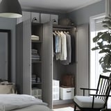 A modern gray wardrobe with open doors revealing clothes and shelves, integrated lighting, and a hanging rod, demonstrating organized storage space.