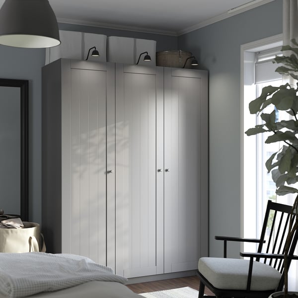 Large white PAX wardrobe against blue wall, near bed, chair, and plant.