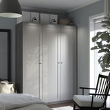 Large white PAX wardrobe against blue wall, near bed, chair, and plant.