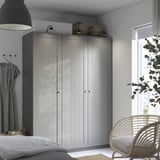 Modern bedroom with large grey PAX closet, wicker chair, and plant. Wardrobe is tall, reaching ceiling, with woven baskets on top.