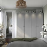Minimalist bedroom: large grey PAX wardrobe, white lamp, green bed cover, white side tables.