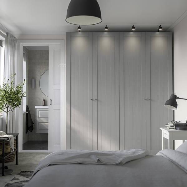 Modern bedroom with gray PAX wardrobe, doorway to bathroom, bed, desk lamp & plant.