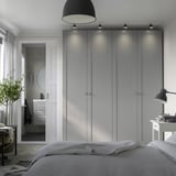 Modern bedroom with gray PAX wardrobe, doorway to bathroom, bed, desk lamp & plant.