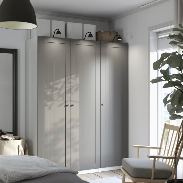 Modern bedroom with large PAX wardrobe in gray, wood chair, bed, and lamp. Wardrobe stands tall, towering over other items.