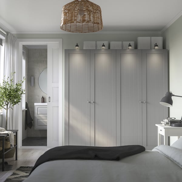 Modern bedroom with tall gray PAX wardrobe & white attached bathroom, featuring sleek design, integrated lighting, and a black desk lamp.