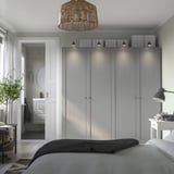 Modern bedroom with tall gray PAX wardrobe & white attached bathroom, featuring sleek design, integrated lighting, and a black desk lamp.