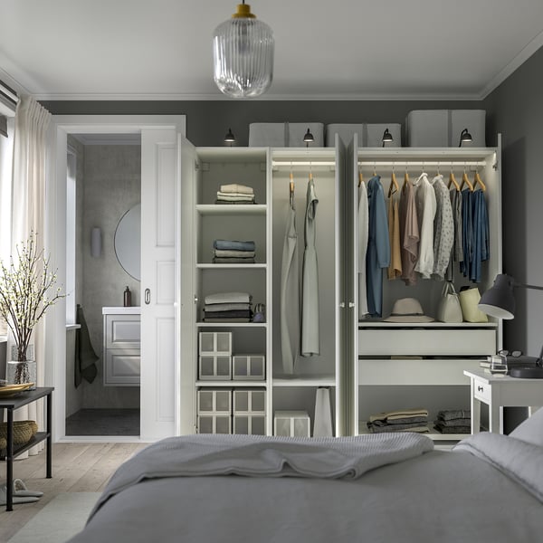 Modern bedroom with open wardrobe, displaying clothes and shelves, next to bathroom.