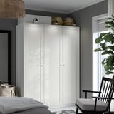Large white PAX wardrobe stands tall, spanning the room height, flanked by wicker baskets and subtle lighting, near a window with plants.