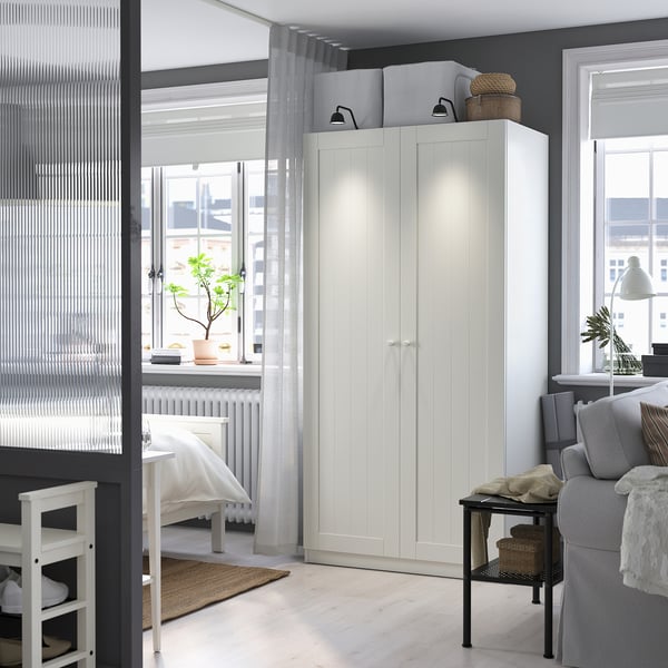 Modern living room with white PAX wardrobe near window, grey curtains, sofa, and small plant on windowsill. Bright and cozy decor with neutral tones.