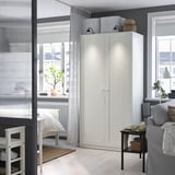Modern living room with white PAX wardrobe near window, grey curtains, sofa, and small plant on windowsill. Bright and cozy decor with neutral tones.