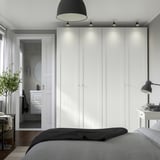 Modern bedroom a large white PAX wardrobe with integrated lighting, dark pendant lamps, and a black and grey bed. Wardrobes size dominates the space.