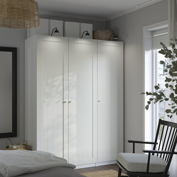 Modern bedroom with tall white PAX wardrobe & black rocking chair. Wardrobe is large, surrounded by smaller items.