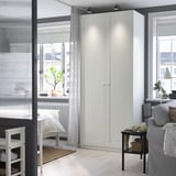 A white PAX wardrobe between window & wall, beside grey sofa, clean & organized.