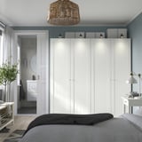 Minimalist bedroom with large white PAX wardrobe against blue wall, modern decor, and open doorway to en suite.