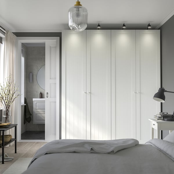 Modern bedroom: large white PAX wardrobe with integrated lighting, gray bed, and gray bathroom through doorway.