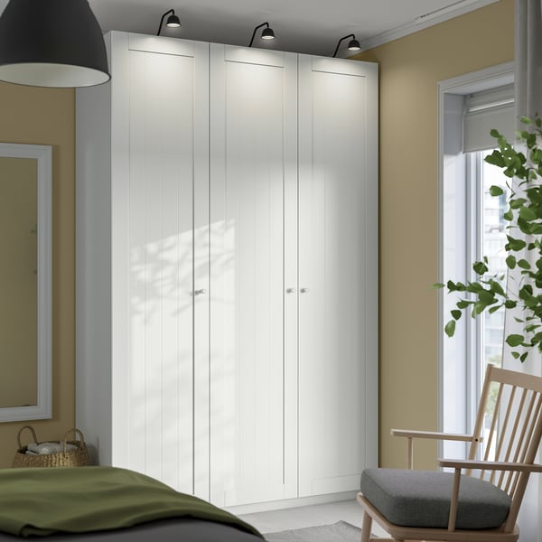 White PAX corner wardrobe in cozy room with green bed, wooden chair by window.