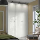 White PAX corner wardrobe in cozy room with green bed, wooden chair by window.