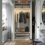 Modern wardrobe organizes clothes with hanging rail, shelves, and basket for storage. Soft-closing hinges visible, adjustable feet for floor leveling.