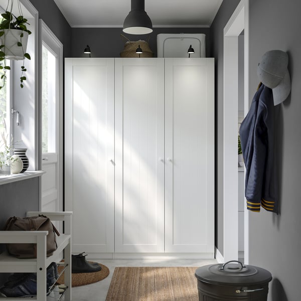 White wardrobe in corner with lamp, bench, and navy coat.