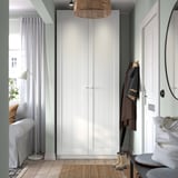 Modern entrance with tall white PAX wardrobe, jacket, boots, mirror, grey sofa, lamp, and window.