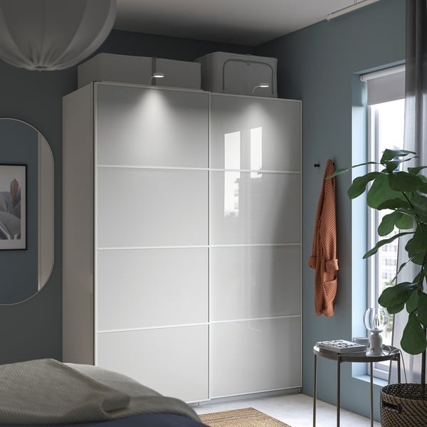 Modern bedroom with sleek gray PAX wardrobe featuring sliding doors and built-in lights, next to a bed with white linens and a side table with plants.