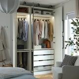 Open wardrobe with clothes, drawers, bins, and mirror doors reflecting a room with a bed and window.