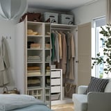 A modern closet with folding clothes, shelves, and storage bins, fixed to wall, near a bed and chair.
