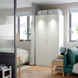 Modern bedroom with large white floral-patterned PAX wardrobe, green armchair, wooden table, and bed by window. Wardrobe and armchair dominate space.