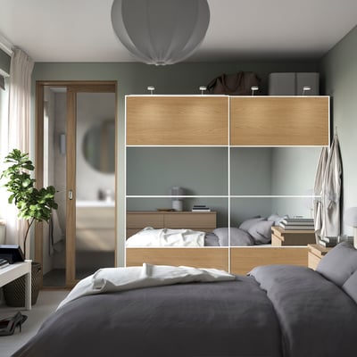 Modern bedroom with PAX wardrobe, bed, plant, and mirror.