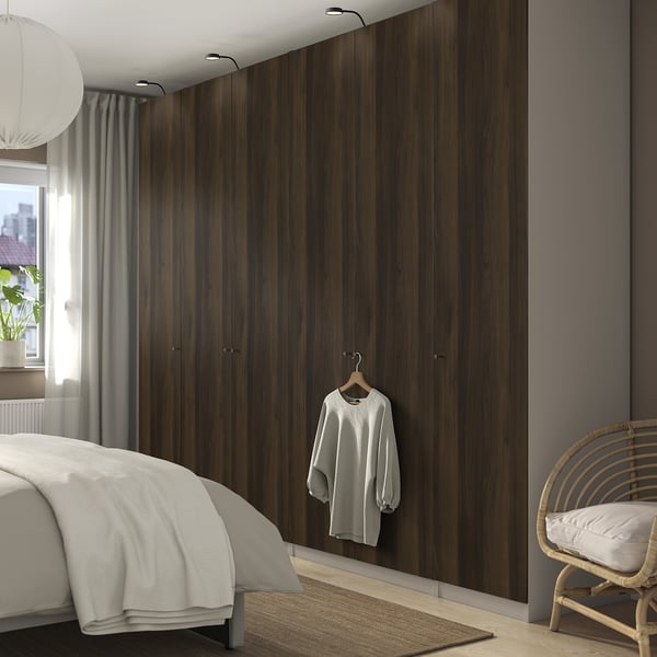 Modern bedroom with large brown PAX wardrobe, white sweater, cozy bed, wicker chair, rug, and ceiling lamp.