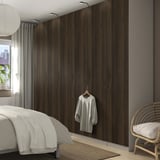 Modern bedroom with large brown PAX wardrobe, white sweater, cozy bed, wicker chair, rug, and ceiling lamp.