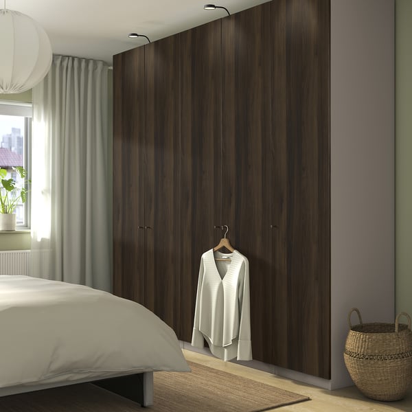 Modern bedroom with tall, dark PAX wardrobe, white bed, pendant lamp, green curtain, and wicker basket.