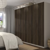 Bedroom with dark wooden PAX wardrobes, mesh baskets, soft-close hinges, and decorative lights. Bed partially visible.